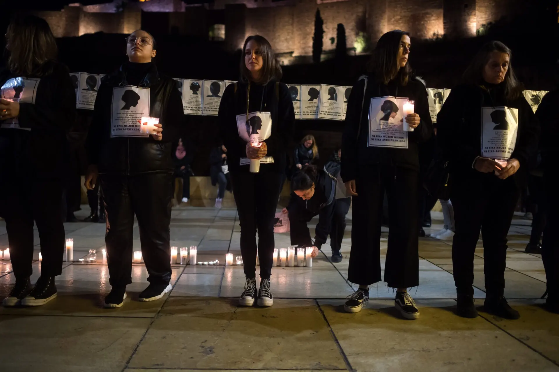 A woman is seen placing a candle on a street as others stand