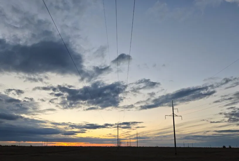 Power lines and electricity pylons stretch across a vast field under a dramatic sunset sky, Kazakhstan